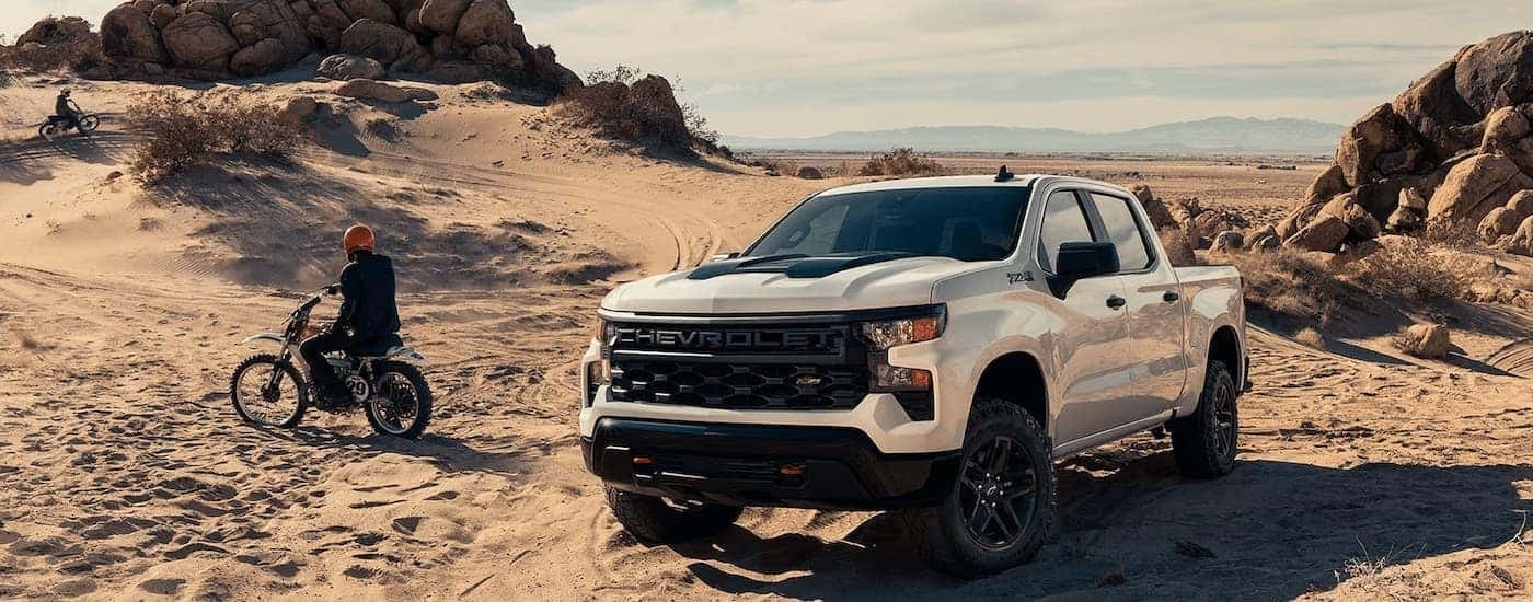 A white 2024 Chevy Silverado 1500 Custom Trail Boss is parked on a sandy trail.