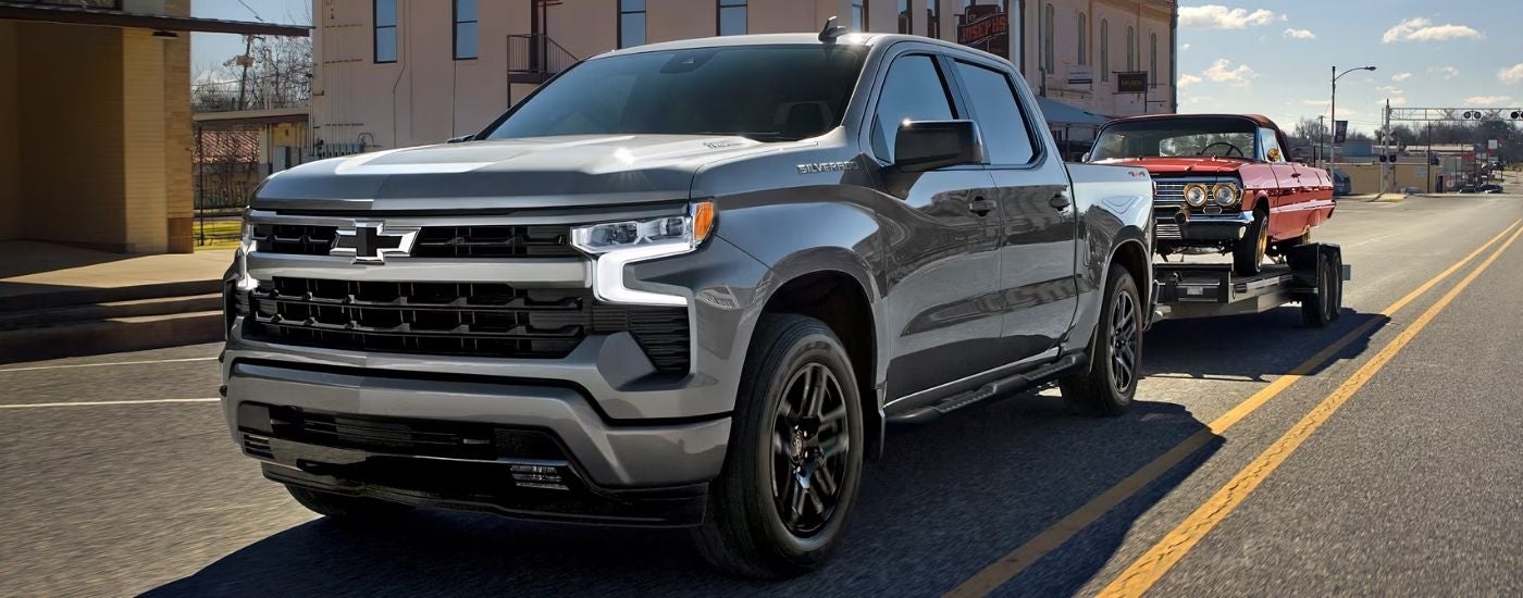 Silver 2026 Chevy Silverado 1500 RST towing a car on a trailer