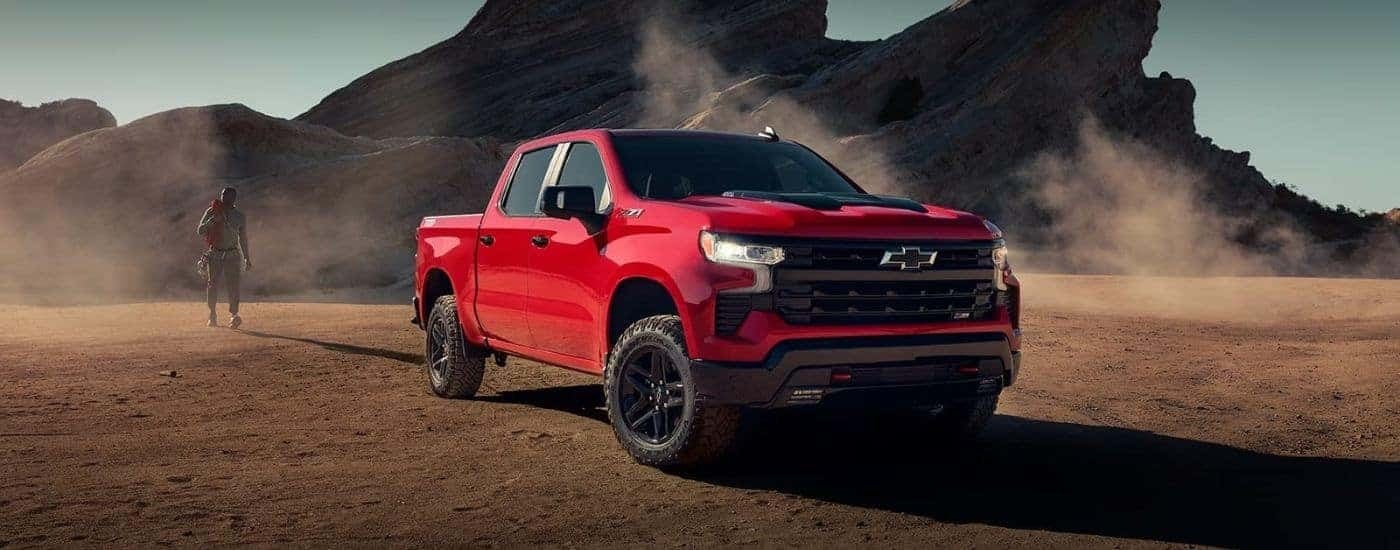A red 2024 Chevy Silverado 1500 LT Trail Boss parked in front of a rocky outcropping.