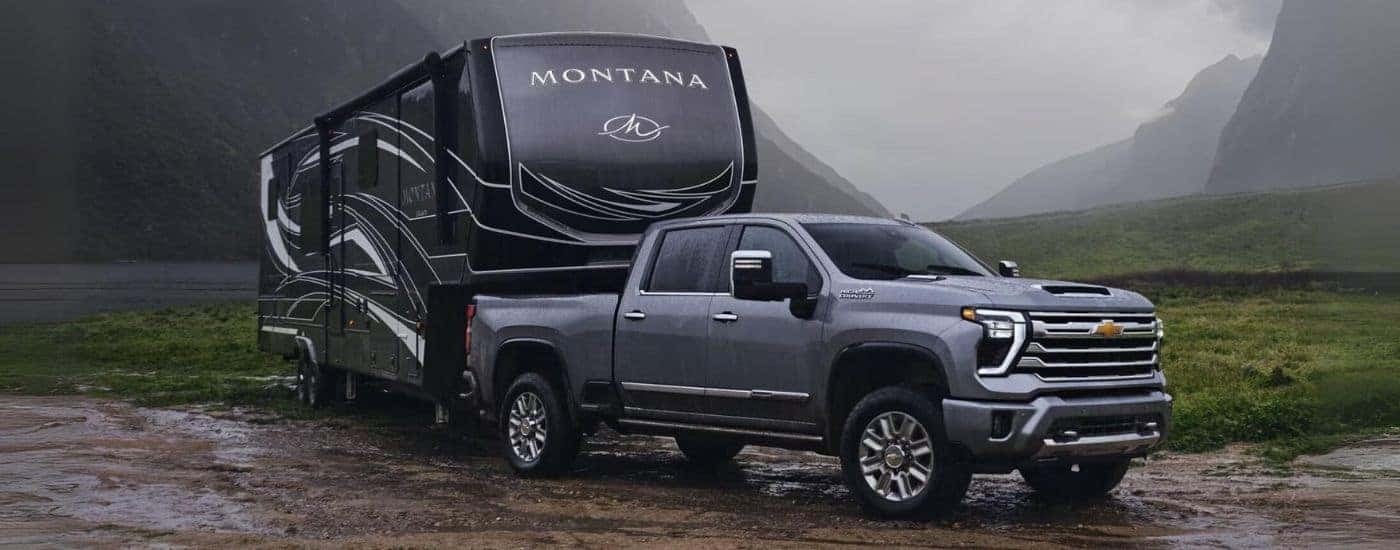 One of the most popular trucks for sale in Birmingham, a grey 2024 Chevy Silverado 2500 HD High Country, is shown towing a camper