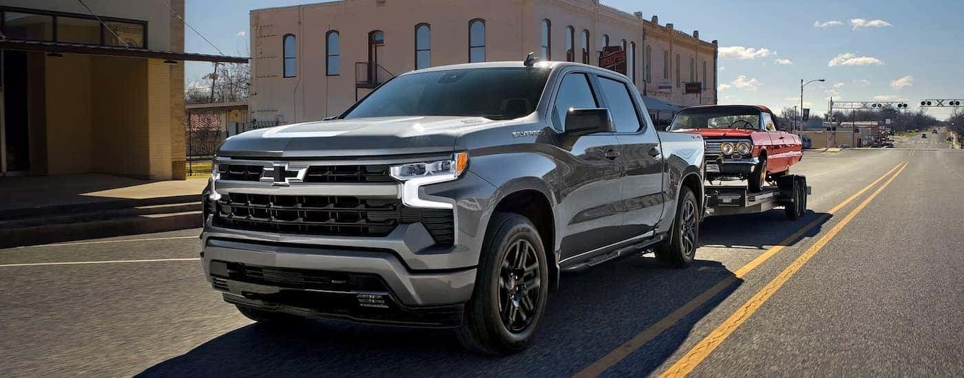 Silver 2026 Chevy Silverado 1500 towing a red vehicle on a trailer