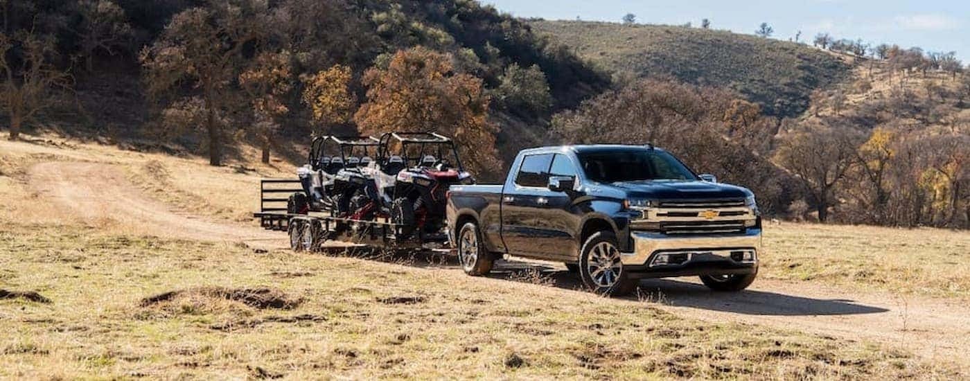A black 2020 Chevy Silverado 1500 is shown towing a trailer with UTVs on it.