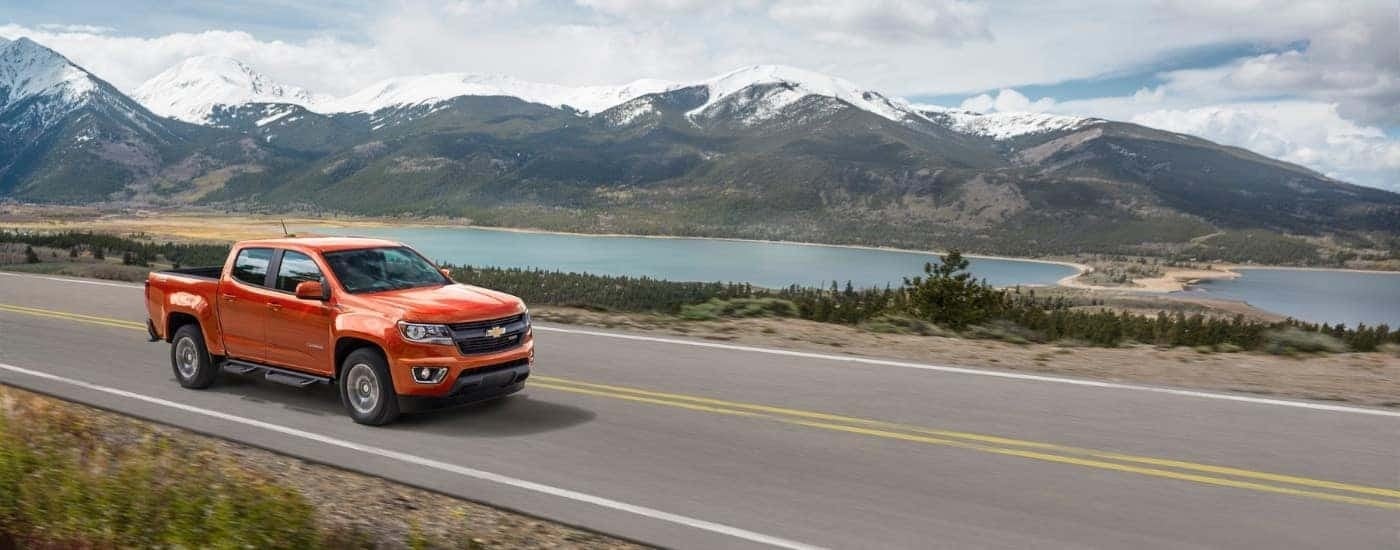 An orange 2016 Chevy Colorado Z71 is shown driving past a lake and mountains after leaving a used Chevy truck dealer near you.